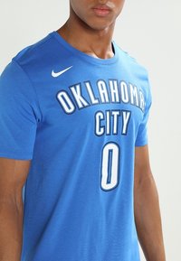 Niebieska koszulka Oklahoma City z białymi literami. Posiada okrągły dekolt, krótkie rękawy oraz graficzny numer "0" na plecach. Wykonana z miękkiej bawełny.