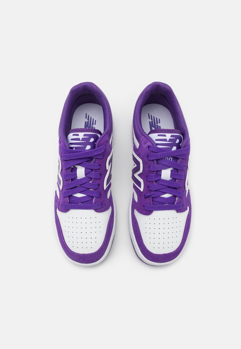 Baskets de sport violettes et blanches avec un dessus en tissu texturé, fermeture lacée, bout perforé et logo visible sur la languette.