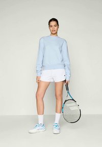 Felpa azzurra chiara, pantaloni corti bianchi, scarpe da ginnastica bianche e calzini bianchi. Tiene in mano una racchetta da tennis con un accento blu. Design semplice.