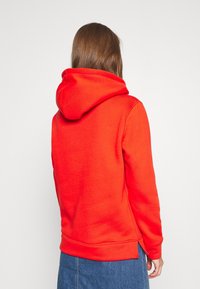 Felpa rossa con tessuto testurizzato, cappuccio regolabile e polsini a costine. Presenta una silhouette dritta e fessure laterali all'orlo.
