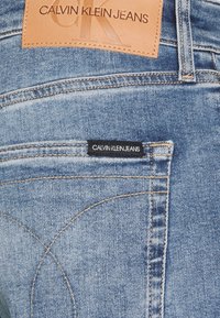 Jasnoniebieskie jeansy z denimu z naszywką ze skóry oznaczoną napisem „CALVIN KLEIN JEANS” oraz kontrastującymi przeszyciami, z detalem tylnej kieszeni i gładką fakturą.