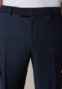 Marineblauwe op maat gemaakte broek met een gestructureerde stof, een vlakke voorkant en riemlussen, voorzien van subtiele gestikte accenten langs de tailleband.