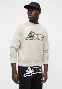 Ανοιχτό γκρι φούτερ με γραφικό μαύρης γάτας, λαιμόκοψη σε στυλ crew και ριμπ στα μανίκια. Συνδυάζεται με μαύρα τζιν που έχουν περίγραμμα λευκής γάτας.