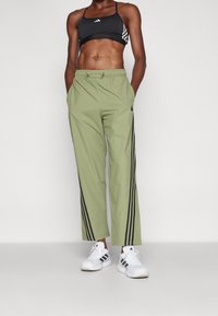 Zelené zúžené kalhoty s černými bočními pruhy, elastickým pasem a lehkým materiálem. V kombinaci s černým sportovním podprsenkou a bílými teniskami.