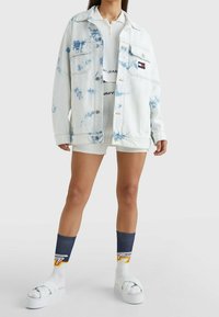 Hellblaues Batik-Jeansjackett mit lockerer Passform, großen Taschen und silbernen Details. Getragen über einem weißen Strickoberteil und Shorts.