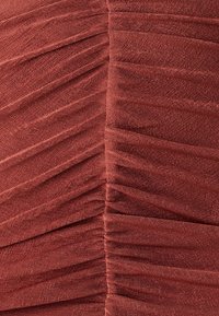 Ruched fabric dress in deep rust color, showcasing horizontal pleats and a textured finish, emphasizing a body-hugging silhouette.
