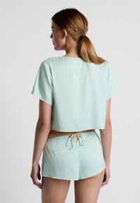 Mintgroen cropped top met korte mouwen, voorzien van een subtiel patroon. De bijpassende shorts hebben een elastische tailleband en een strikdetail.