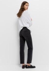 Zwarte high-waisted jeans met een rechte pasvorm, gemaakt van denim. Gecombineerd met een witte langwerpige top en zwarte schoenen.
