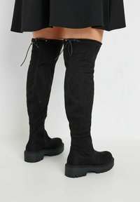 Svarta mocka stövlar över knäet med en platt, strukturerad sula, snörning upptill och dragkedja på sidan för enkel påtagning.