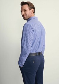 Niebieska i biała koszula w kratę zapinana na guziki z długimi rękawami, w połączeniu z granatowymi spodniami i czarnym paskiem, pokazana od tyłu.