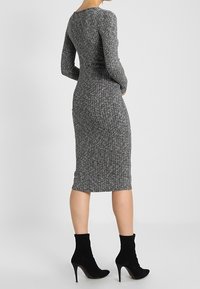 Abito a coste grigio con maniche lunghe e silhouette aderente, che arriva a metà polpaccio, abbinato a stivaletti neri alla caviglia. Design minimalista.