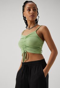 Zelený ribbed crop top s nariaďovaním a šnúrkou na spodnom leme, spárovaný s voľnými čiernymi nohavicami s bočnými vreckami.