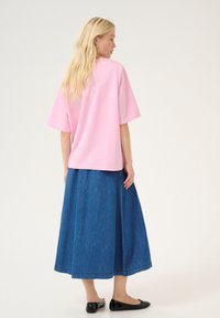 Roza bombažna oversize majica s kratkimi rokavi, v kombinaciji z dolgo modro denim krilo. Obleko dopolnjujejo ravni črni čevlji.