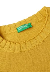 Gul stickad tröja med ribbad rundhals. Lappen visar "United Colors of Benetton" på en grön bakgrund.