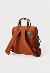 Zaino in tessuto arancione con accenti in pelle marrone, doppi manici superiori, spallacci imbottiti e un portachiavi decorativo attaccato.