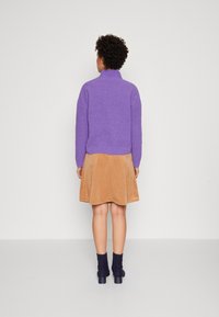 Violetti neulepusero korkealla kauluksella, yhdistettynä vaaleanruskeaan samettihameeseen ja tummansinisiin tekstuuri-sukkahousuihin mustojen, paksukorkoisten kenkien kanssa.