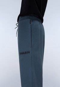 Gray sweatpants made of soft fabric, featuring an elastic waistband with drawstring, side pocket, and a black logo on the left thigh.