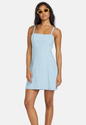 Vestido de mezclilla azul claro con tirantes finos, diseño ajustado, dobladillo a la altura de la rodilla y detalles de costura sutiles. Acompañado de gafas de sol amarillas.