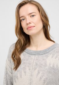 Jasnoszary sweter dzianinowy z żebrowanym dekoltem. Posiada teksturowany wzór oraz miękki, lekki materiał. Subtelna wariacja kolorystyczna w całej powierzchni.