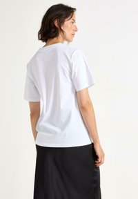 Hvid bomulds t-shirt med korte ærmer, rund halsudskæring og en afslappet pasform. Bæres med en sort nederdel, der fremhæver en glat tekstur.