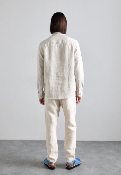 Chemise en lin beige clair à manches longues, assortie à un pantalon beige et des sandales bleues. Design simple, finition en tissu texturé.