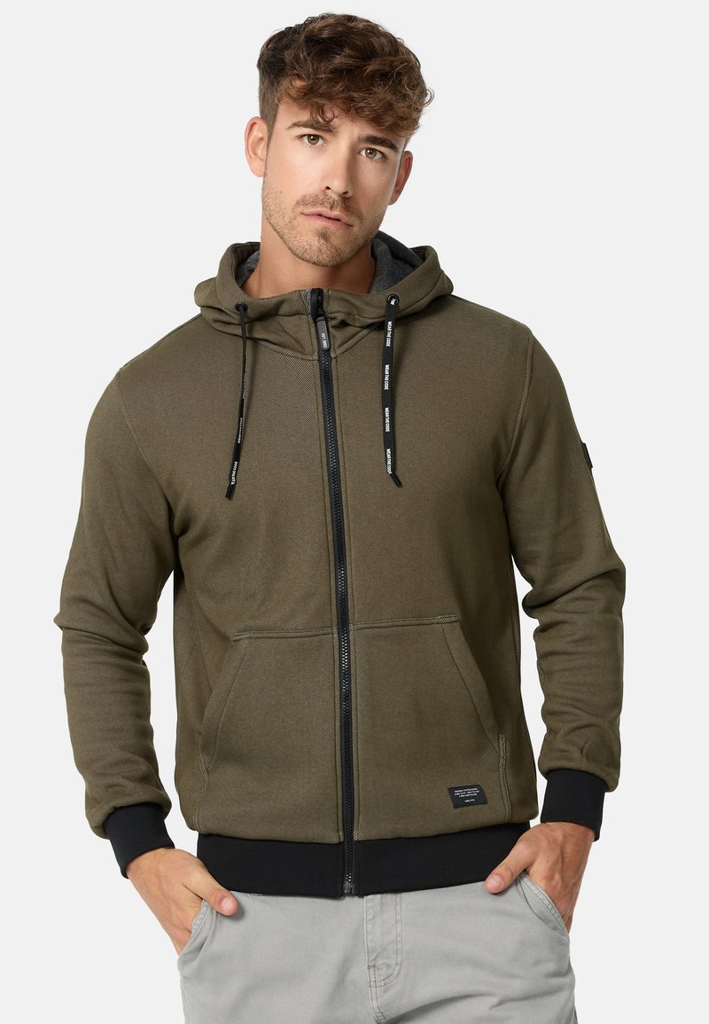 Olivegrüner Reißverschluss-Hoodie aus weichem Material, mit Kapuze, Fronttaschen, schwarzen Akzenten und verstellbaren Kordeln an der Kapuze.