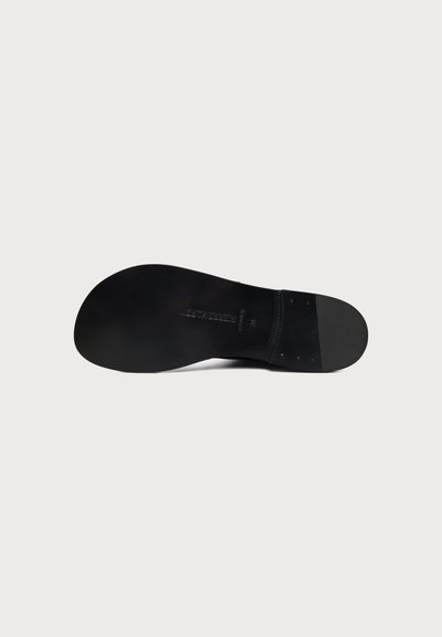 Semelle de chaussure en cuir noir avec texture lisse et petit texte de marque en relief au centre, présentée sur fond blanc.