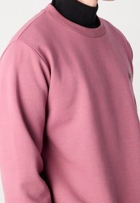 Felpa rosa in misto cotone; presenta una scollatura tonda e un piccolo logo sul petto. Tessuto strutturato con finitura morbida.