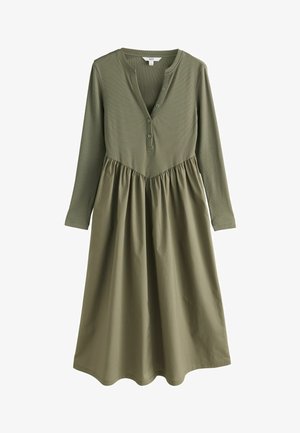 Ilgomis rankovėmis alyvuogių žalia suknelė su mygtukais užsisegančiu V formos kaklu ir rinkta sijonu, sujungiant juostelės ir lygios medžiagos tekstūras. Banguota apatinė dalis.