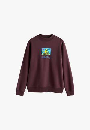 Bluza bordo cu guler rotund, manșete rib, și un design brodat multicolor Keith Haring pe piept.