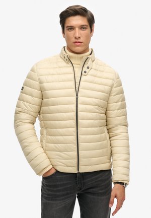 Beige puffer jacket with horizontal stitching, high collar, front zipper, and knit cuffs, worn over a cream turtleneck sweater.