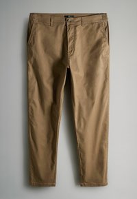 Pruunid chinod, mis on valmistatud puuvillase segukangast, on varustatud küljetaskutega, nupukinnitusega ja kohandatud jala kujuga. Sile tekstuur.