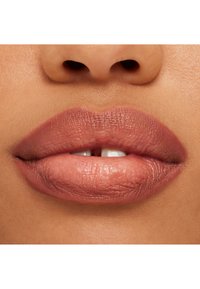 Pintalabios nude mate en labios llenos y suaves. Textura sutil con un brillo natural, mostrando un contorno ligeramente más oscuro a lo largo de los bordes.