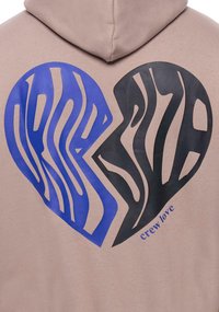 Brauner Hoodie mit einem Herzgrafik, das in Blau und Schwarz geteilt ist, mit gewellten Linien. Darunter steht der Text "Crew love" in Blau. Weiche, glatte Textur.