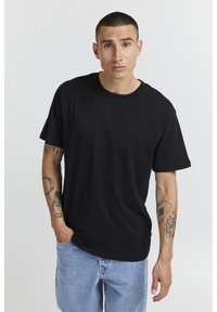 Black cotton t-shirt with a crew neck. Short sleeves, relaxed fit, smooth texture, paired with light blue denim shorts. Minimalistic design.
