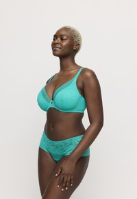 Reggiseno in pizzo color teal con scollatura profonda e motivi decorativi, abbinato a slip in pizzo coordinati. Spalline regolabili e texture liscia.