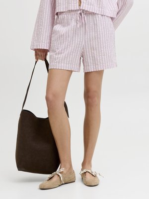 Donna che indossa pantaloncini a righe rosa e top, con una grande borsa a tracolla marrone scuro, e ballerine beige con fiocchi di nastro.