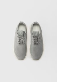 Baskets en tricot gris avec des motifs texturés, conception à lacets et un tirant au talon. Semelle blanche douce et branding subtil sur la languette.