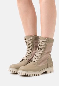 Beige Kampfstiefel mit einer glatten Lederfront und einem Stoffoberteil, ausgestattet mit einer Schnürdesign und einer robusten Gummisohle mit ausgeprägtem Profil.