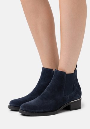 Bottes cheville en daim bleu marine avec panneaux latéraux élastiques, design élégant, talon carré et sans ferrures visibles. Texture lisse avec une silhouette moderne.