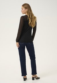 Juodas viršus su permatomomis ilgomis rankovėmis ir vertikaliais grioveliais, derinamas su tamsiai mėlynomis džinsais ir juodais aukštakulniais bateliais su bloku.