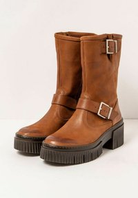 Brown leather ankle boots with a wide, flared black rubber sole, silver buckle accents, and a smooth textured finish.