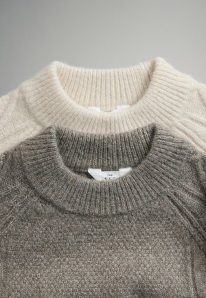 Két pulóver bordázott nyakkivágással, az egyik bézs, a másik szürke. Mindkettő puha kötött anyagból készült, finom textúrával. Címkék láthatóak.