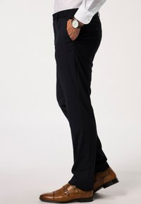Pantalones a medida en azul marino oscuro con dos bolsillos laterales, combinados con una camisa blanca. Zapatos de monk strap dobles de cuero marrón, que muestran líneas elegantes y un minimalismo en los detalles.