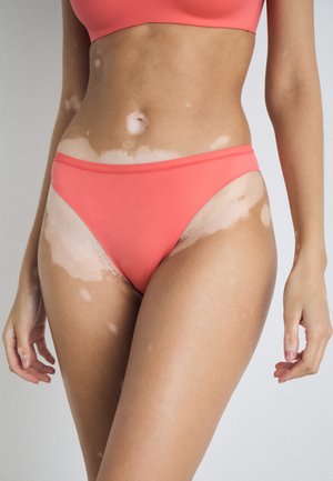Bas de bikini corail en tissu doux, présentant un design minimaliste avec une taille fine et une ouverture de jambe haute.