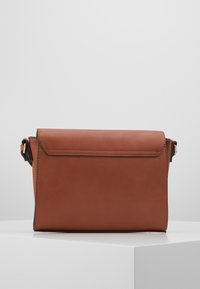 Borsa a tracolla rettangolare in pelle marrone con chiusura a patta, bordi neri e tracolla regolabile, posizionata su un piedistallo bianco.