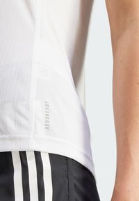 Weißes Sporttanktop aus strukturiertem Meshmaterial mit "AEROREADY"-Branding. Kombiniert mit schwarzen Shorts mit weißen Streifen.