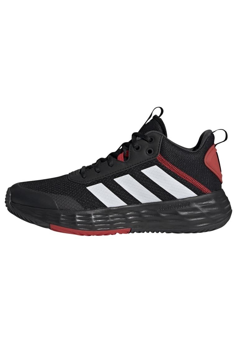 Zapatilla deportiva negra con parte superior de malla transpirable, tres rayas blancas, acentos rojos en el talón y una suela negra texturizada.