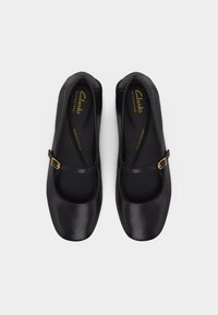 Μαύρα δερμάτινα παπούτσια Mary Jane με χρυσά αγκράφες και μαξιλαροειδείς εσωτερικές σόλες, εμφανιζόμενα από πάνω σε λευκό φόντο.