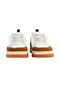 Baskets blanches avec des accents en suède beige, boîtier perforé au niveau des orteils, lacets plats beiges et semelles en caoutchouc orange. Inclut une tirette noire à l'arrière.